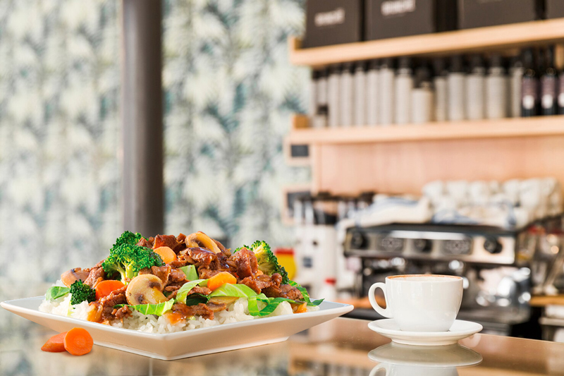 Prato de comida Prato de carne com legumes e arroz servido ao lado de uma chávena de café, em cima de uma montra de vidro